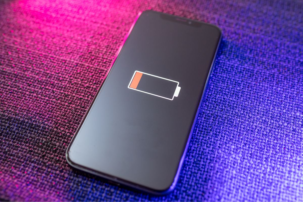 Smartphone affichant une icône de batterie faible sur un fond violet lumineux.
