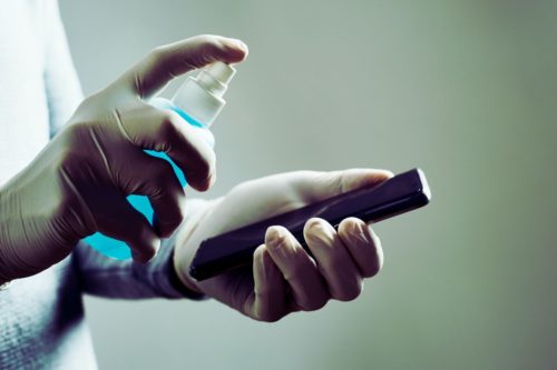 Personne avec des gants désinfectant un smartphone