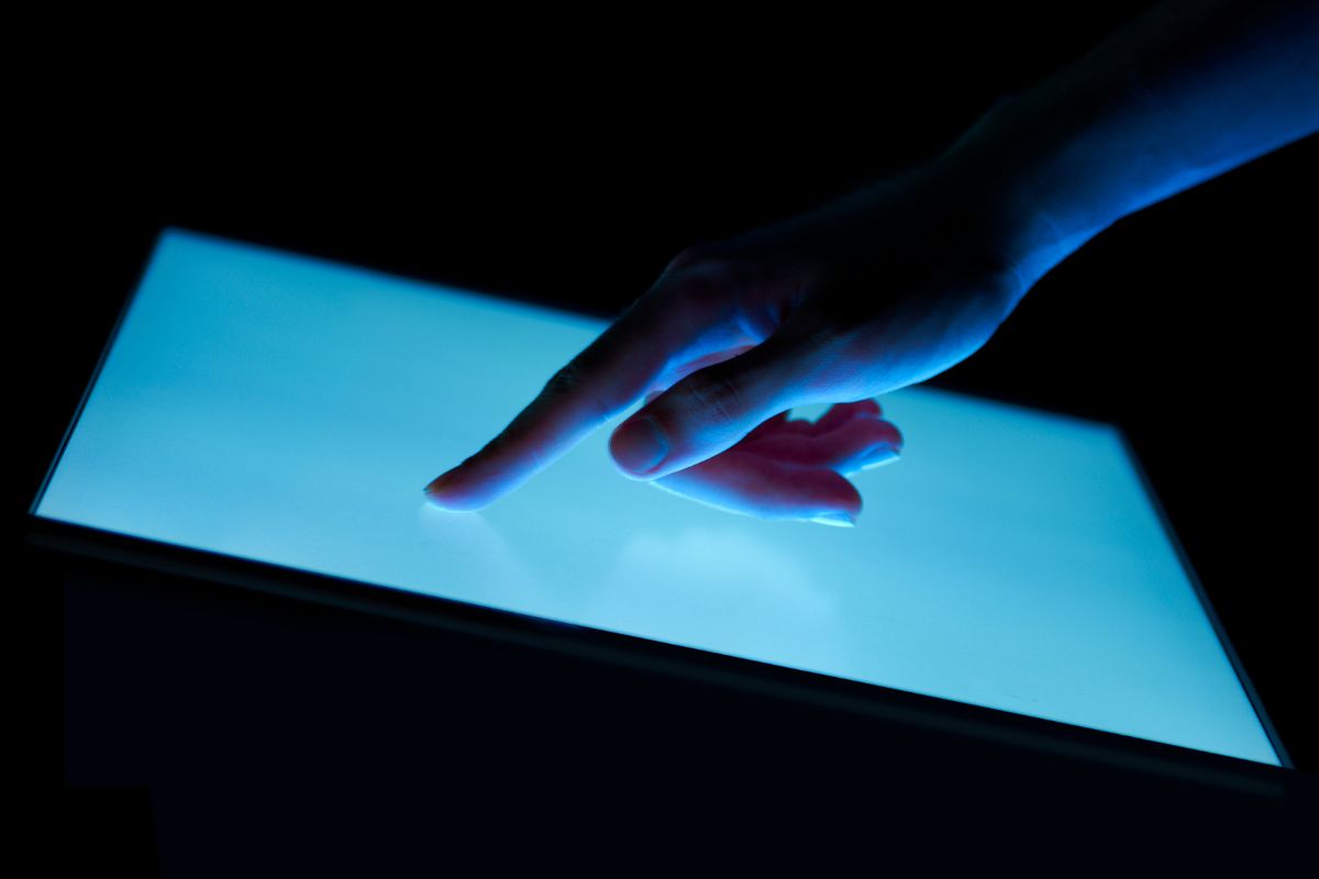 Une main touchant un écran lumineux dans le noir.